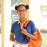 Estudiante dominicana sonriente en su escuela, destacando la importancia de la educación de calidad para romper los ciclos de pobreza y desigualdad en República Dominicana.