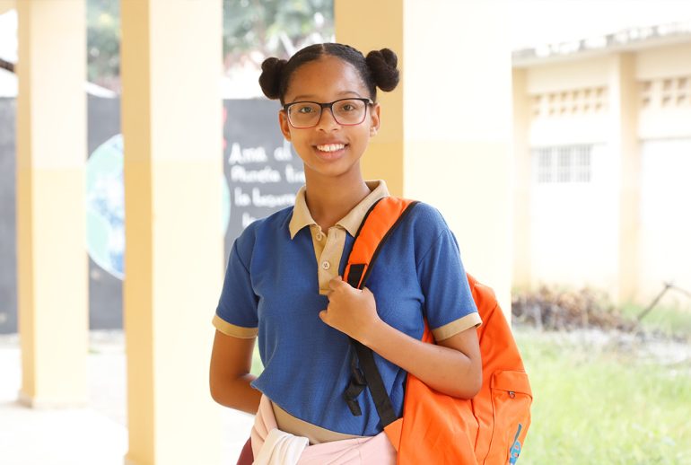 Estudiante dominicana sonriente en su escuela, destacando la importancia de la educación de calidad para romper los ciclos de pobreza y desigualdad en República Dominicana.