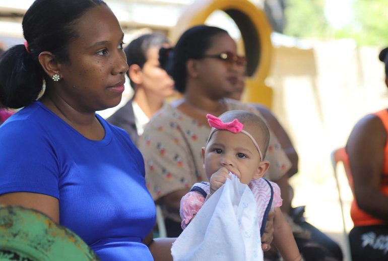 Madre dominicana asistiendo a una sesión informativa sobre lactancia materna con su bebé, destacando la importancia de esta práctica para la salud infantil y la seguridad alimentaria.